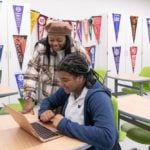 Teacher helping student on a laptop in a classroom