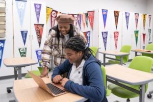 Teacher helping student on a laptop in a classroom