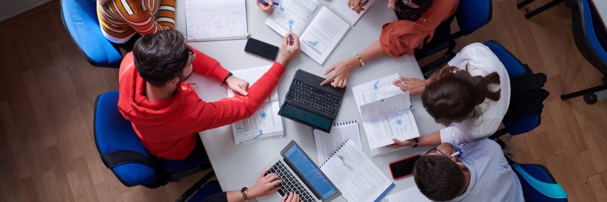 Top view of university students sitting at a table studying and working on laptop